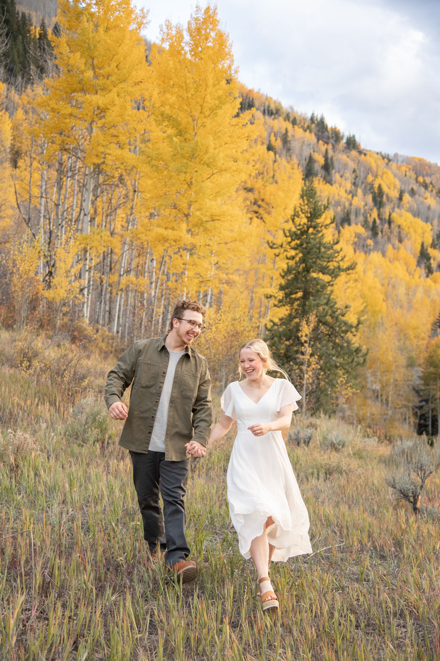 a cute couple frolicking in a field with fall background for engagement photos in Vail Colorado