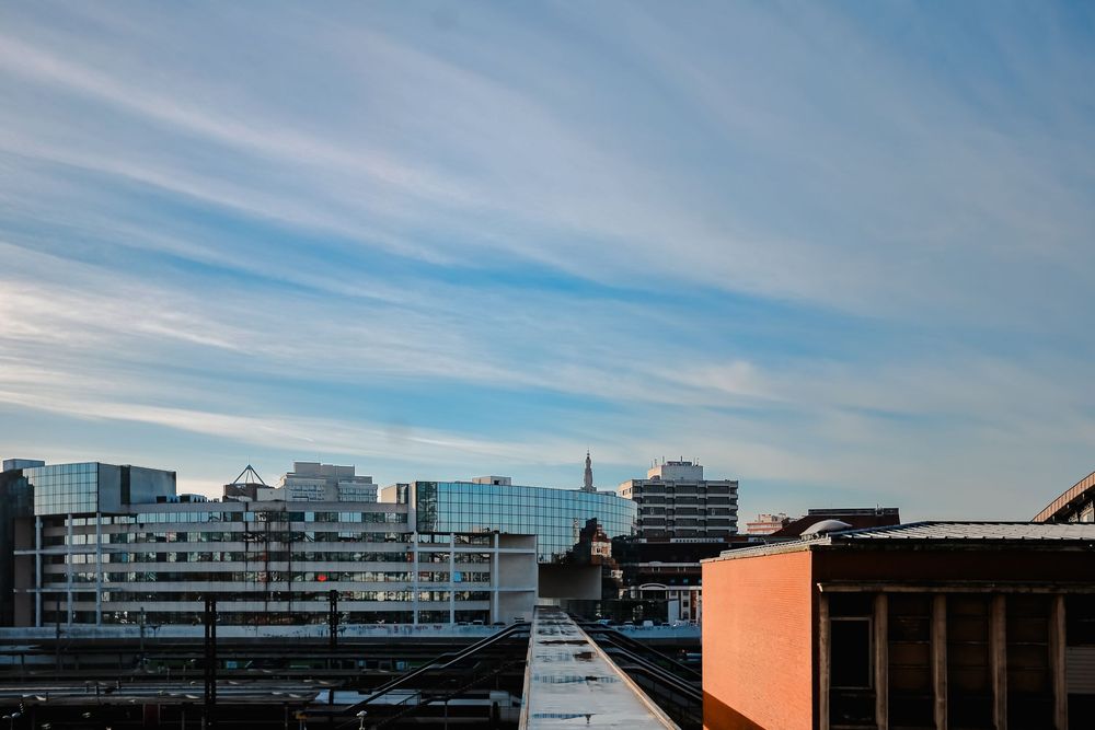 Panoramic urban skyline view under a blue sky with wispy clouds from a rooftop perspective.