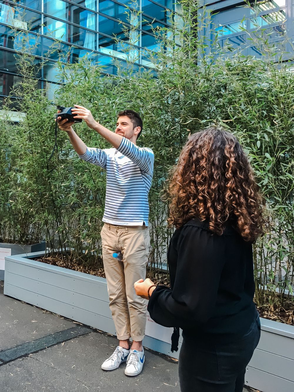 Male student taking a photo with a camera outdoors near bamboo plants on a business school campus.