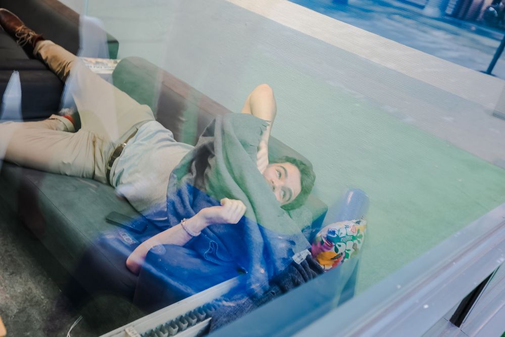 Student relaxing on a couch, lying down with colorful accessories in a casual campus setting.