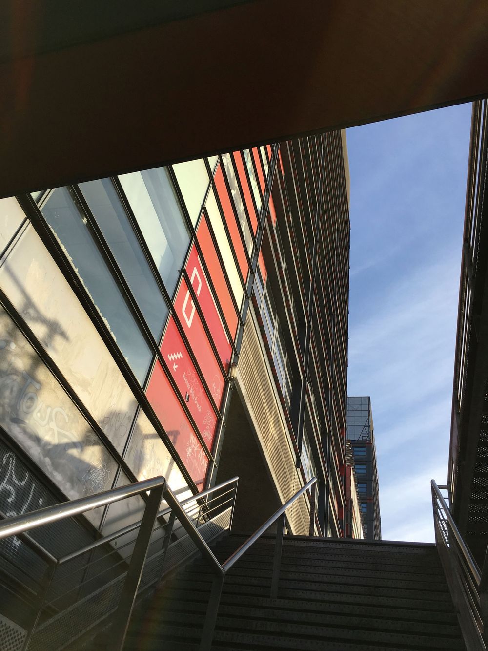 Upward view of modern glass and red-paneled building facade against a clear blue sky.
