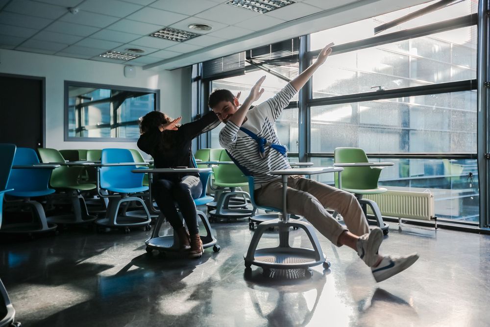 Two students playfully spinning on modern wobble chairs in a bright, contemporary SKEMA classroom.