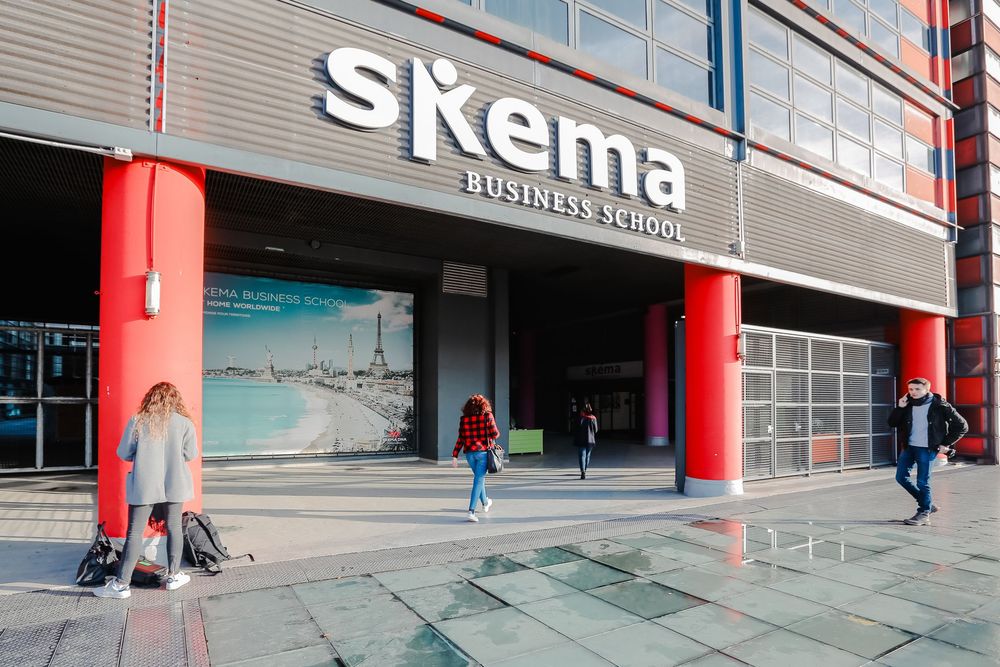 Students walking outside the modern SKEMA Business School building with striking red columns.