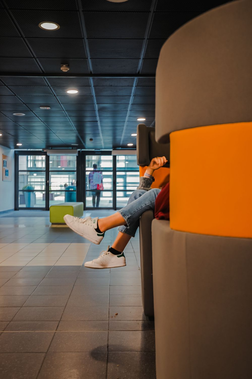Student relaxing in an orange pod chair with legs stretched out in a modern school hallway.