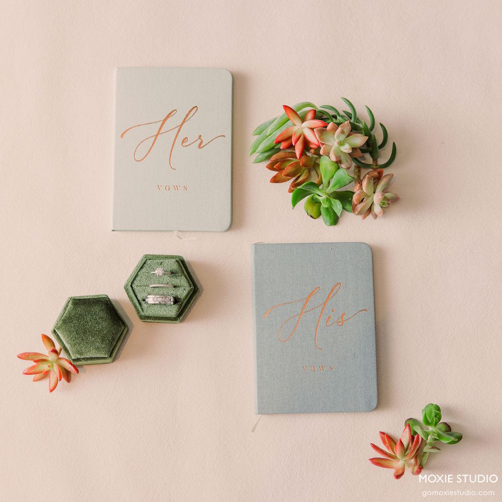 Elegant wedding stationery flatlay with sage green tiles, coral flowers, and hexagonal glass details on beige background.