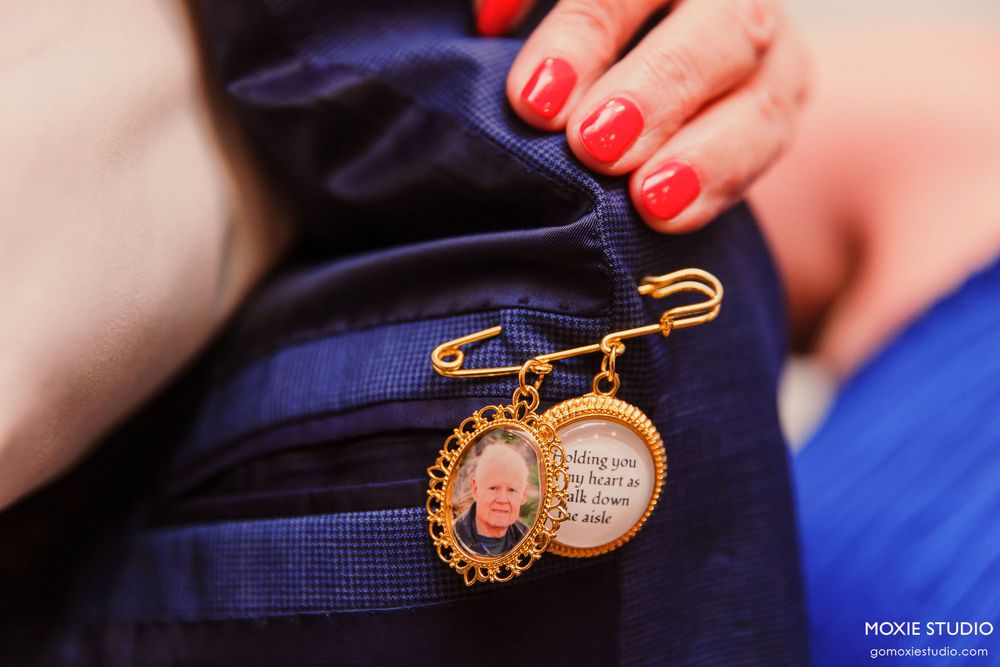 A close-up of hands with red nail polish holding a vintage-style locket pin against a navy blue fabric.
