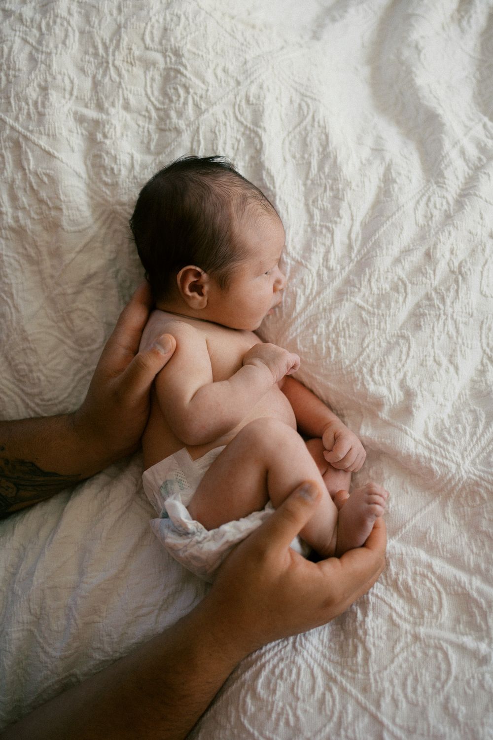 Newborn baby lying on white textured bedding in a sequence of gentle movements.