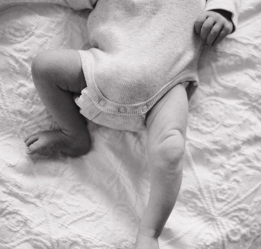 Close-up black and white photo of a newborn baby swaddled in soft white fabric on textured bedding.