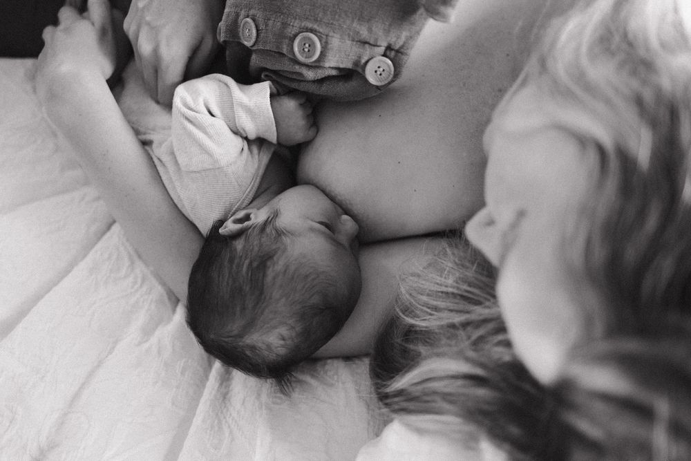 Intimate black and white photograph of parent and newborn sharing a tender moment on white bedding.