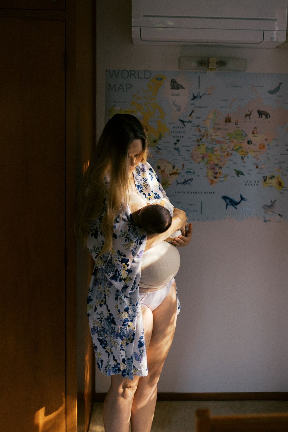 A world map hangs on a wall while someone stands in front of it during golden hour lighting.