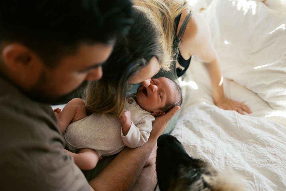 Artistic black and white portrait of parent and baby lying together on white textured blanket.