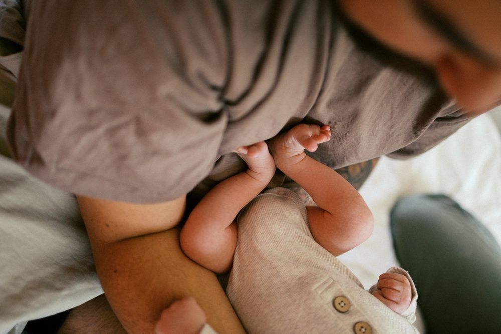 Overhead view of tiny baby feet and hands being gently held against soft gray fabric.
