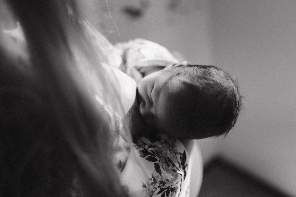 Black and white close-up photo of a newborn baby being held against someone's chest.