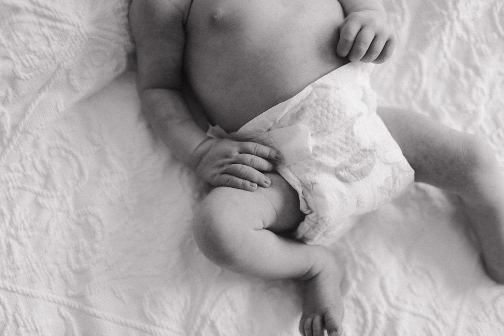 High contrast black and white image of an infant lying on white bedding with tiny hands resting on their belly.