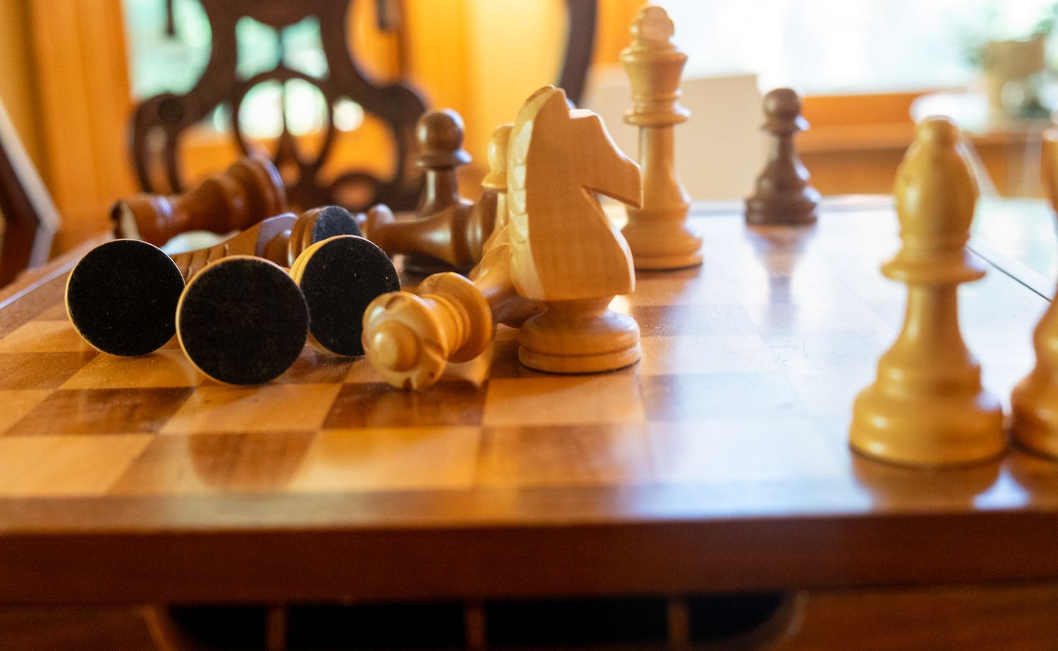 Chess pieces scattered on a wooden chessboard with dramatic lighting highlighting the game pieces.