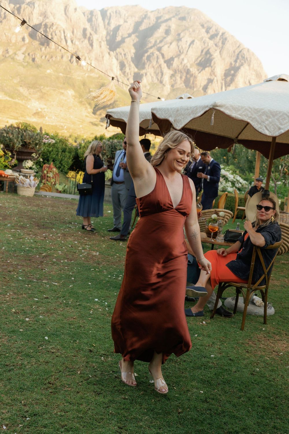 A sequence of photos showing a person in a burgundy dress dancing joyfully on grass at an outdoor event.