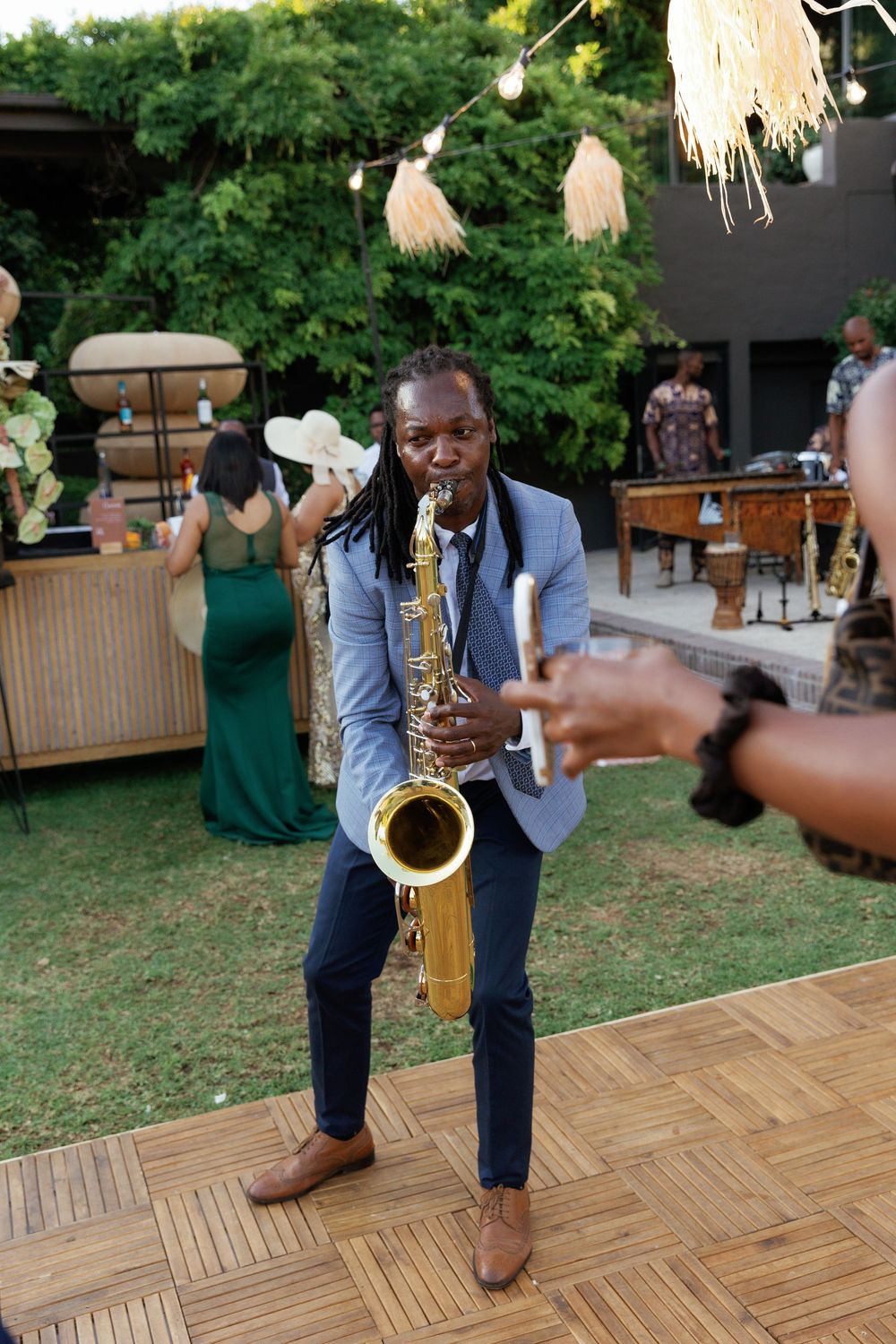 A person dances on a wooden floor at an outdoor event with string lights and umbrellas visible in the background.