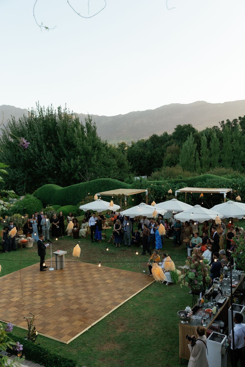 An outdoor wedding reception venue with a checkered dance floor and white umbrellas at dusk.