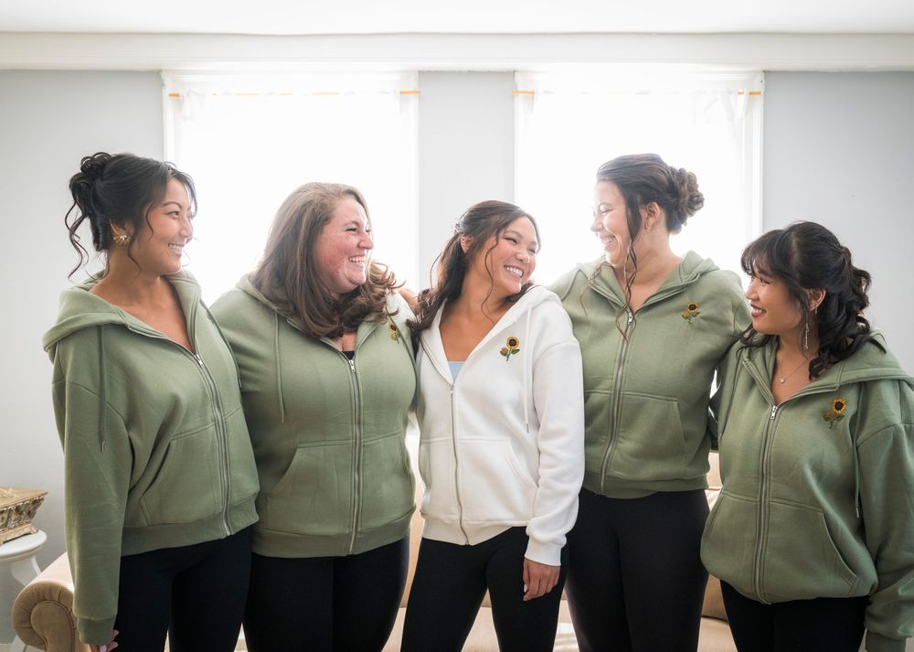 Group of people in olive green and white clothing stand together in a white room during a casual gathering.