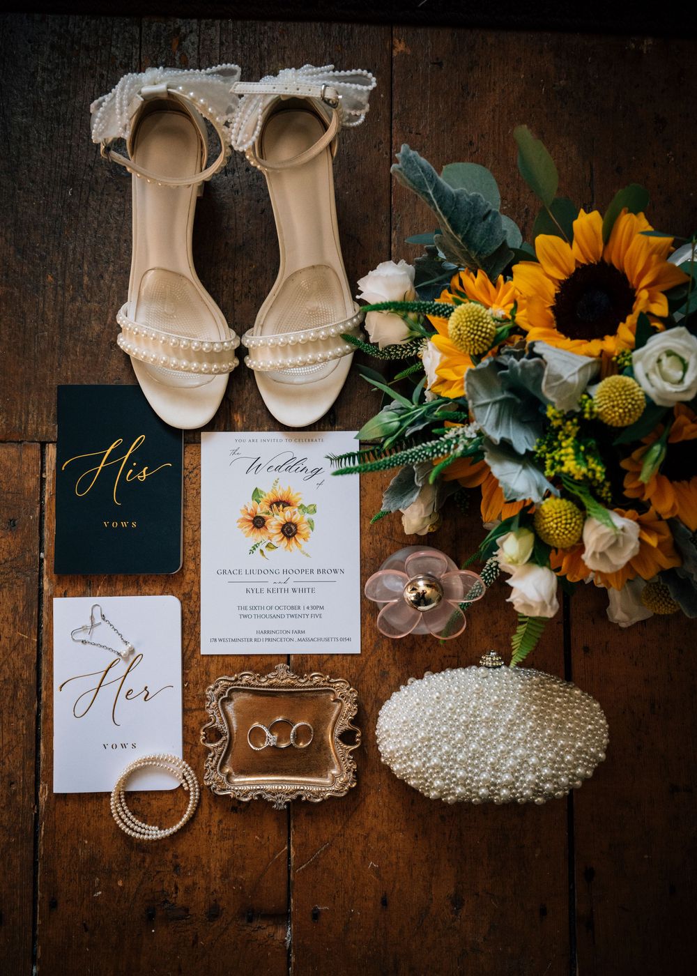 Wedding detail flatlay with sunflowers, pearl accessories, invitations and cream colored shoes on rustic wooden surface.