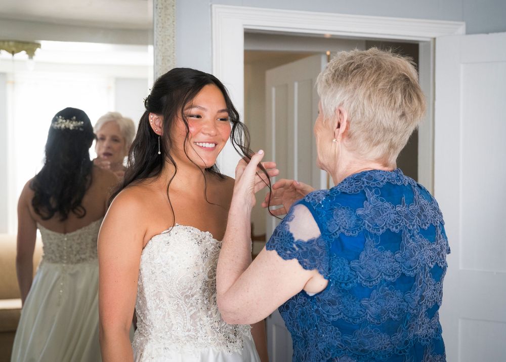 A bride in a white strapless gown shares an emotional moment with a woman in a blue lace dress during wedding preparations.