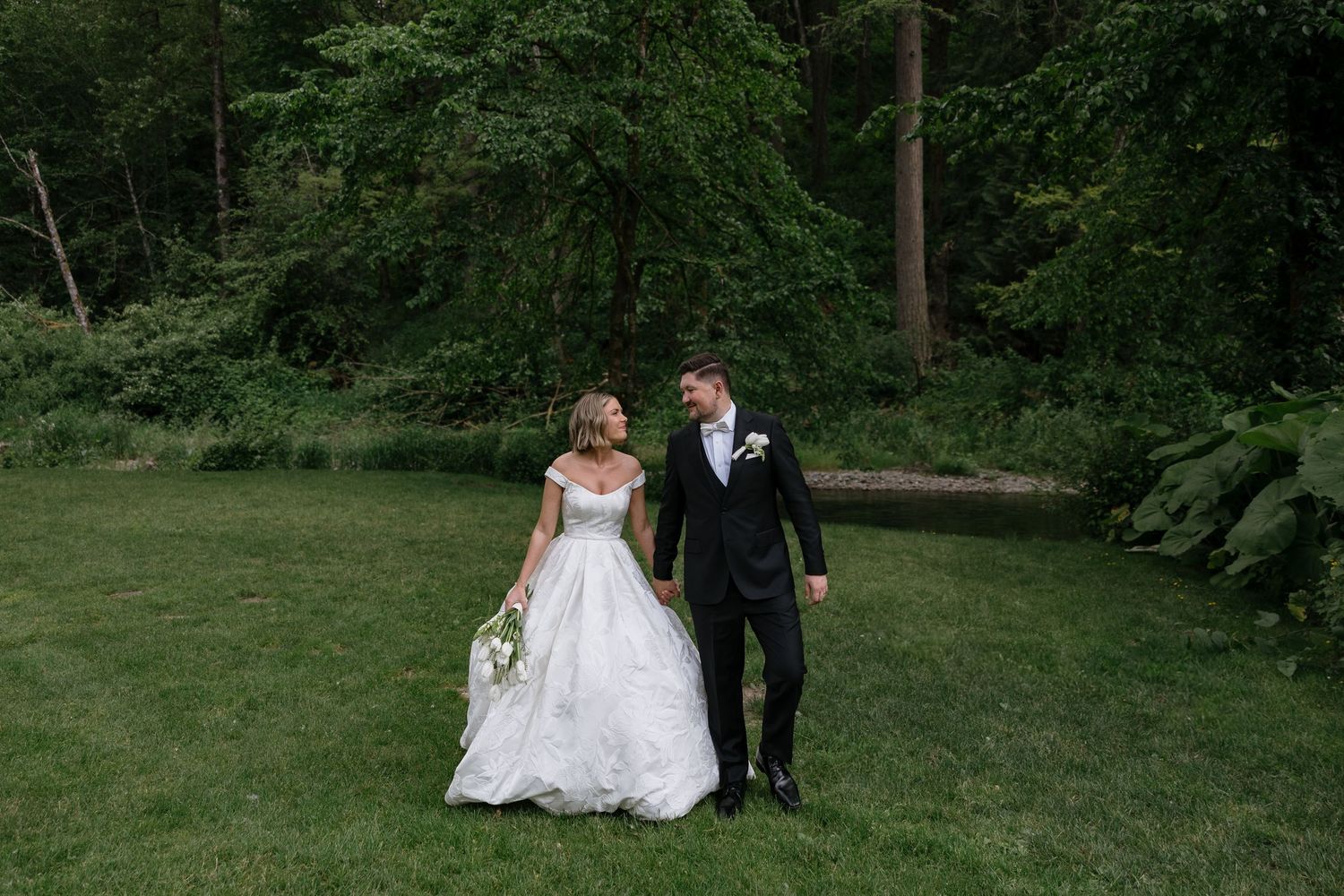 A couple in wedding attire shares a romantic moment in a lush green garden setting.