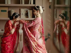 Three people in traditional red and gold Indian wedding attire pose elegantly in a room.