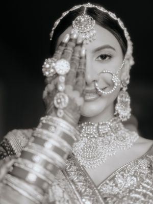 Black and white portrait of a bride in traditional South Asian wedding attire with ornate jewelry and henna decorated hands.