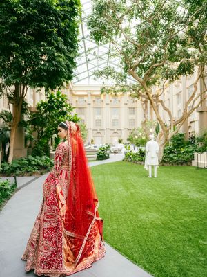 A traditional red and gold Indian bridal lehenga photographed in an elegant greenhouse garden setting with lush greenery.