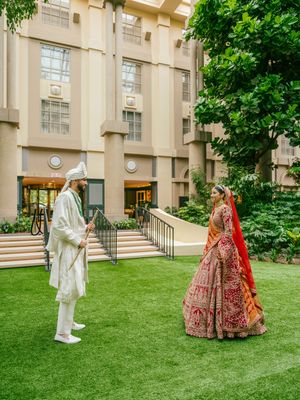 Traditional Indian wedding ceremony outdoors with ornate red and white attire on a green lawn.