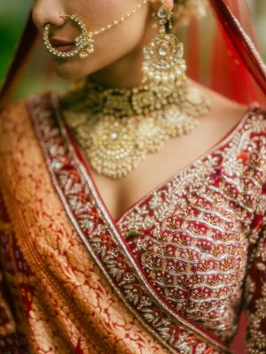 Close-up detail of ornate bridal jewelry and red embroidered lehenga with intricate beadwork and traditional Indian design.