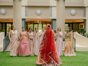 Wedding party wearing pink and peach bridesmaid dresses poses on lawn outside elegant building.
