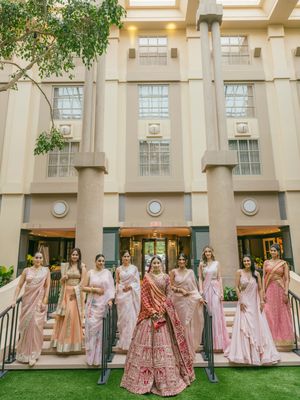 A wedding party in pink and blush toned outfits poses on steps of a beige building with columns.