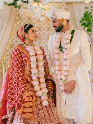 A couple in traditional South Asian wedding attire share romantic moments during their ceremony with pink floral decor.