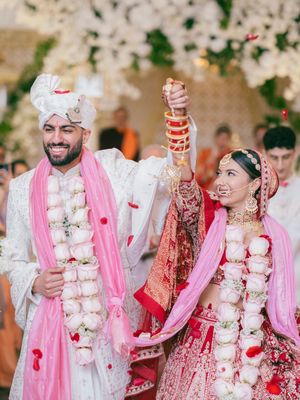 A traditional Indian wedding ceremony with the couple wearing ornate pink and white floral garlands and traditional attire.
