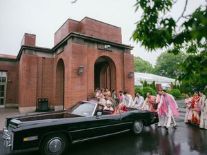 A black vintage convertible car parked outside a brick building with people gathered around it in the rain.