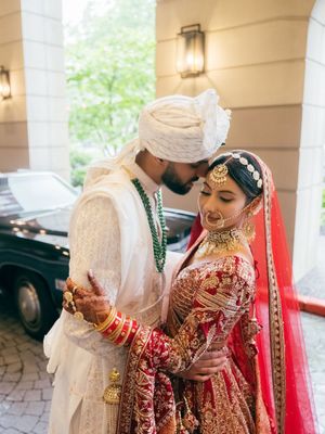 A couple in traditional South Asian wedding attire performs a ceremony ritual under an elegant covered entrance.