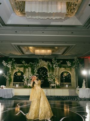 A couple in elegant gold attire performs a romantic dance move in a luxurious ballroom setting.
