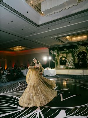 A golden lehenga twirls gracefully on a black and white patterned dance floor during a wedding celebration.