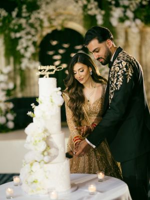 A couple in formal attire cuts their elegant white wedding cake adorned with flowers during their reception celebration.