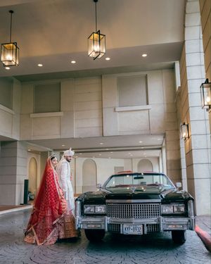 A panoramic view of a luxury wedding venue with vintage Cadillac cars and elegant red decor under pendant lighting.