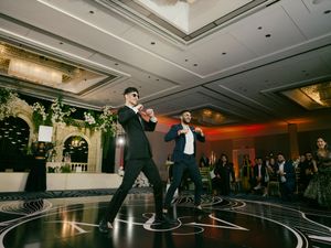 Wedding guests dancing energetically on a circular black and white patterned dance floor at an indoor reception.