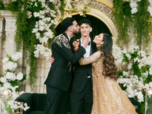 A wedding couple embraces under an elegant stone archway adorned with cascading white floral arrangements.
