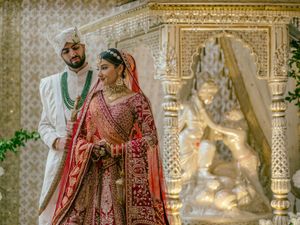 Traditional Indian wedding couple in ornate outfits stand beside an intricately decorated mandap during their ceremony.