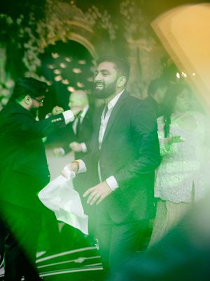 Wedding party dancing under green and blue lighting effects on a monochrome dance floor.