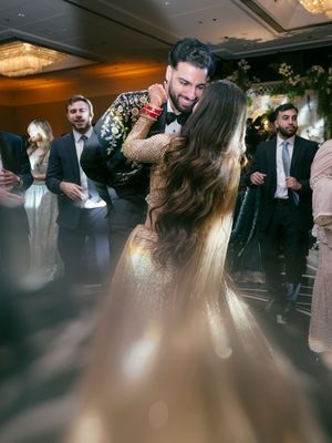 Guests gather in a dimly lit ballroom with elegant chandeliers and decorative greenery overhead.