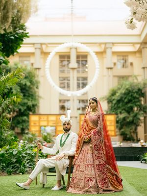 Wedding couple in traditional South Asian attire pose together on manicured lawn with elegant building backdrop.