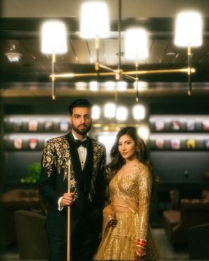 A couple in formal attire poses together under modern pendant lighting in an elegant indoor setting.