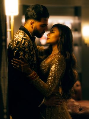 A couple in elegant attire dances intimately in a dimly lit ballroom with romantic golden lighting.