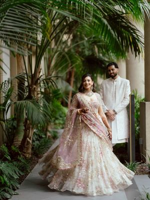 A couple in elegant wedding attire twirls in a garden courtyard surrounded by palm fronds.